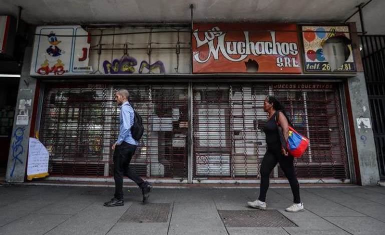 Transeuntes pasan frente Los Muchachos, uno de los 370.000 comercios que han cerrado en Venezuela desde 1998